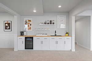 Indoor wet bar with butcher block counters, white cabinetry, open shelves, light carpet, and wine cooler