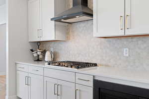 Kitchen featuring range hood, tasteful backsplash, white cabinetry, light stone counters, and stainless steel gas stovetop
