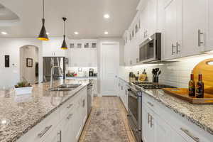 Kitchen with stainless steel appliances, glass insert cabinets, white cabinets, arched walkways, and recessed lighting