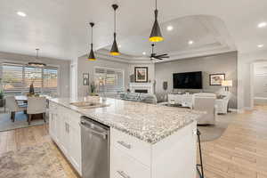 Kitchen with white cabinetry, light stone counters, decorative light fixtures, ceiling fan, and light wood-style flooring