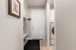Laundry room featuring washer / clothes dryer, cabinet space, and light wood-type flooring