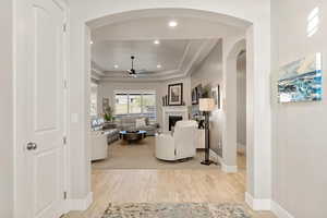 Living area featuring arched walkways, light wood-style floors, a raised ceiling, recessed lighting, and a fireplace