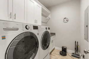 Washroom with light wood finished floors, washer and dryer, electric panel, and cabinet space