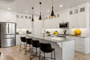 Kitchen featuring light stone counters, appliances with stainless steel finishes, a breakfast bar, a kitchen island with sink, and white cabinetry