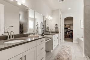 Full bathroom featuring a walk in closet, two vanities, a garden tub, light tile patterned flooring, and recessed lighting