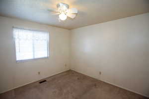 Main bedroom with a textured ceiling, carpet floors, and a ceiling fan