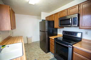 Kitchen featuring electric range oven, stainless steel microwave, light countertops, wood finish cabinetry, and a textured ceiling