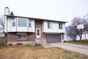 Split foyer home with brick siding, an attached garage, and a front lawn