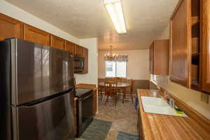 Kitchen with stainless steel appliances, wood finish cabinetry, a chandelier, a textured ceiling, and light countertops