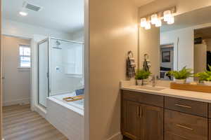 Full bath with a shower stall, light wood-style floors, vanity, and a garden tub