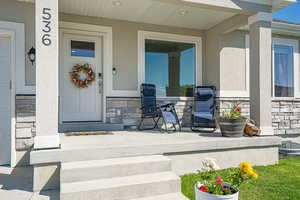Doorway to property with stone siding, covered porch, and stucco siding