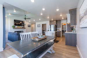 Dining room with vaulted ceiling, light wood-type flooring, ceiling fan, a fireplace, and recessed lighting