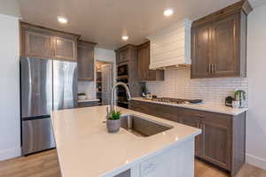 Kitchen with stainless steel appliances, a center island with sink, light wood-style flooring, dark wood finish cabinetry, and light stone countertops