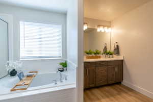 Full bathroom with vanity, a bath, and light wood-type flooring