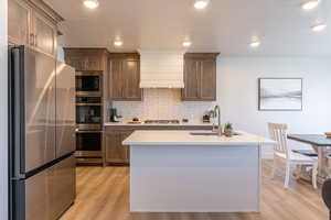 Kitchen featuring stainless steel appliances, light wood-type flooring, recessed lighting, tasteful backsplash, and a center island with sink
