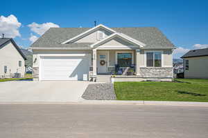 View of front of house with stone siding, covered porch, driveway, and roof with shingles