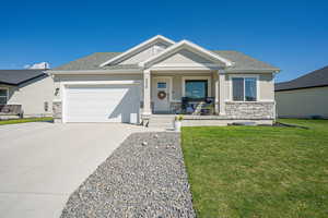 View of front of property featuring stone siding, covered porch, concrete driveway, and roof with shingles