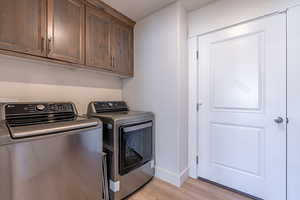 Laundry room with washer and dryer, light wood finished floors, and cabinet space