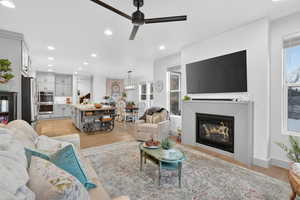 Living room with light wood-style floors, a glass covered fireplace, recessed lighting, a ceiling fan, and healthy amount of natural light