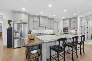 Kitchen with stainless steel appliances, gray cabinetry, light wood-style floors, recessed lighting, and an island with sink
