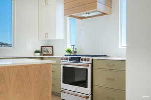 Kitchen featuring white gas range oven, custom range hood, tasteful backsplash, light stone countertops, and green cabinets