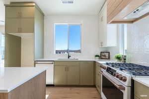 Kitchen featuring gas range oven, custom exhaust hood, tasteful backsplash, dishwasher, and light stone countertops