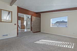 Spare room featuring beam ceiling, a textured ceiling, and carpet floors