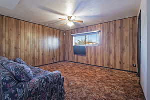 Living area featuring carpet floors, wood walls, a textured ceiling, and a ceiling fan