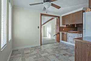 Kitchen featuring stone finish flooring, freestanding refrigerator, ornamental molding, a ceiling fan, and wood finish cabinets