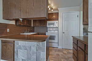 Kitchen featuring white appliances, a peninsula, stone finish flooring, ornamental molding, and backsplash