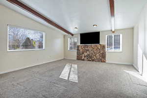 Unfurnished living room with beam ceiling, carpet, and plenty of natural light