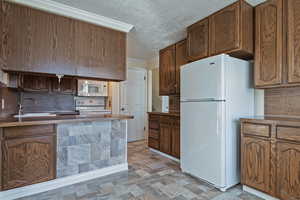 Kitchen featuring white appliances, a textured ceiling, stone finish floors, backsplash, and a peninsula