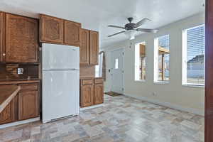 Kitchen with freestanding refrigerator, stone finish floors, wood finish cabinetry, crown molding, and a textured ceiling
