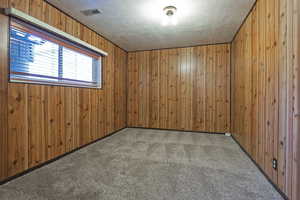 Spare room featuring wooden walls, carpet, and a textured ceiling