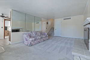 Carpeted living room featuring a stone fireplace, tile patterned floors, a textured ceiling, a ceiling fan, and crown molding