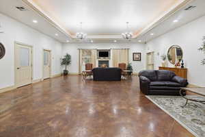 Living room with a raised ceiling, a warm lit fireplace, and suspended lighting