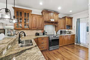 Kitchen featuring wood finish cabinetry, crown molding, stainless steel appliances, glass insert cabinets, and light stone counters