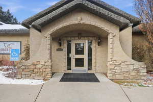 Snow covered property entrance featuring stucco siding and stone siding