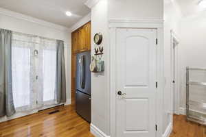 Kitchen with wood finish cabinetry, crown molding, freestanding refrigerator, and light wood-style flooring