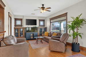Living area with wood finished floors, healthy amount of natural light, ceiling fan, and a fireplace