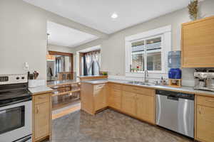 Kitchen featuring appliances with stainless steel finishes, light countertops, light brown cabinetry, a peninsula, and recessed lighting