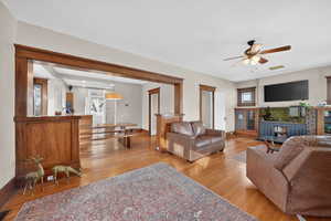 Living area with light wood-style floors, ceiling fan, and a brick fireplace