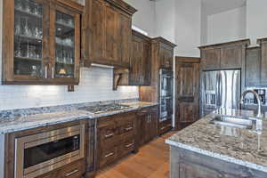 Kitchen featuring light stone countertops, dark brown cabinets, appliances with stainless steel finishes, and light wood-type flooring