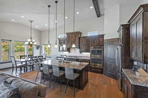 Kitchen with dark stone countertops, hanging light fixtures, dark wood-style flooring, a center island with sink, and recessed lighting