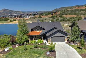 View of front of property featuring concrete driveway, a water and mountain view, stone siding, an attached garage, and a sunroom