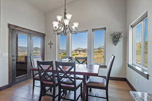 Dining space with dark wood-type flooring, a chandelier, and vaulted ceiling