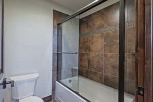 Full bath featuring toilet and combined bath / shower with glass door