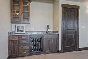 Bar with dark brown cabinetry, light stone counters, carpet, and glass insert cabinets