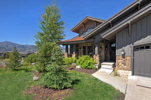 Entrance to property with a lawn, stone siding, covered porch, a mountain view, and board and batten siding