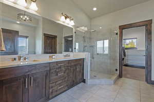 Full bath with double vanity, a shower stall, lofted ceiling, and light tile patterned floors
